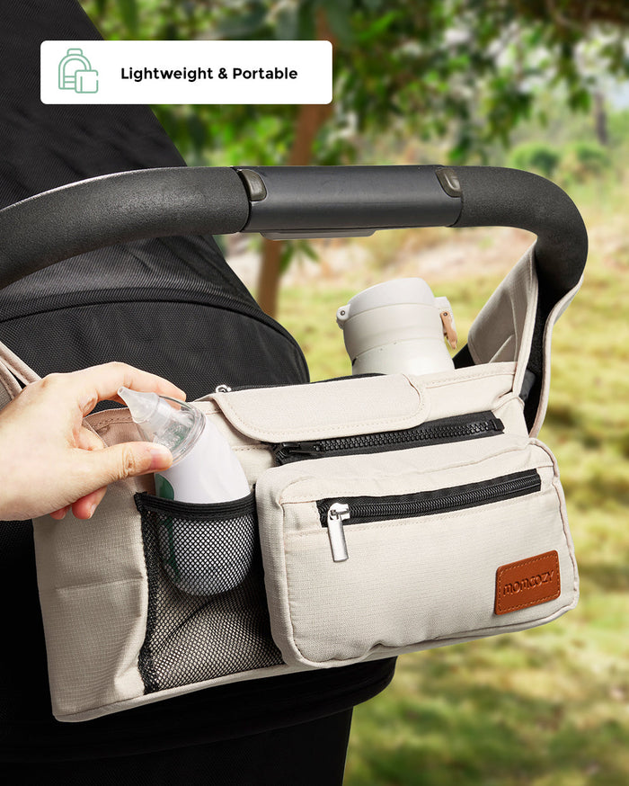 Momcozy stroller organizer bag in beige, with a baby nasal aspirator being placed into a mesh pocket.