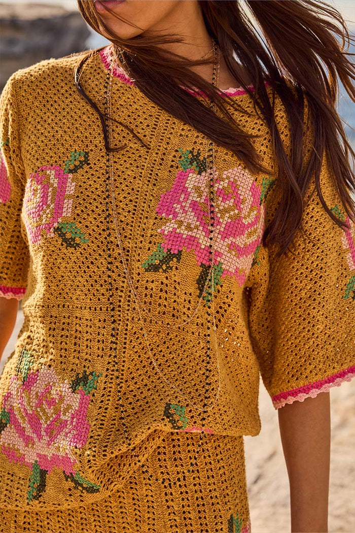 Close-up of mustard knit Coastal Granny Top showing pink floral embroidery and open-stitch texture with scallop trim