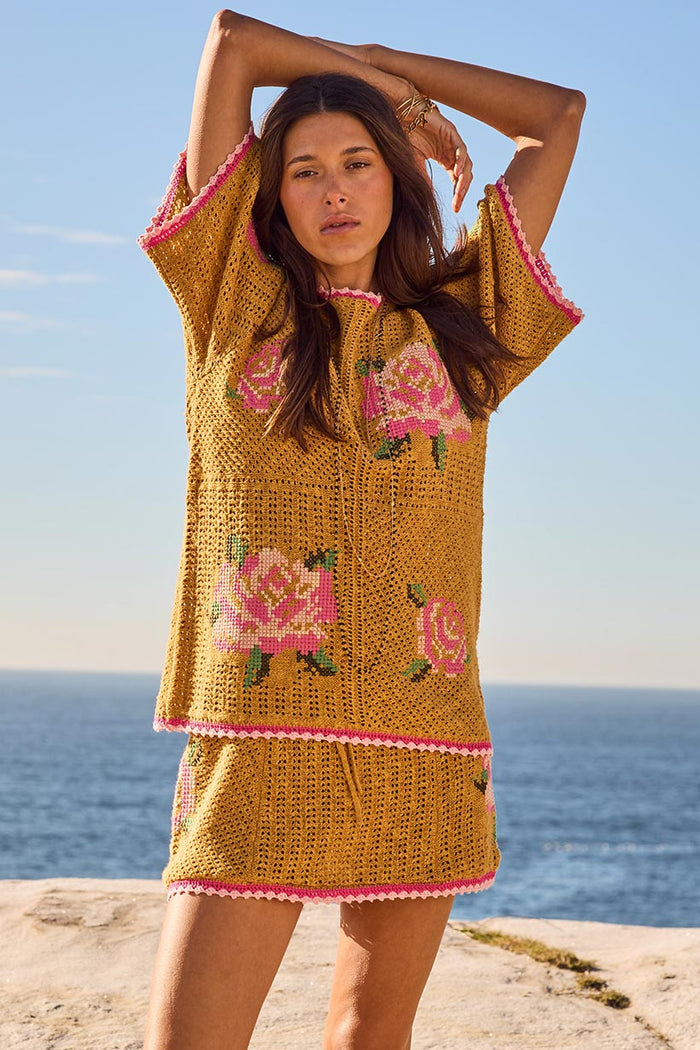 Front view of a model in mustard crochet knit top with pink rose embroidery and scallop trim, paired with matching mini skirt