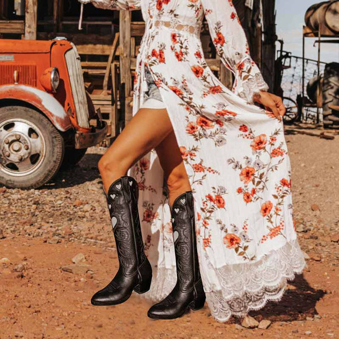 Stylish women's embroidery heart cowgirl boots paired with a floral dress in a rustic outdoor setting